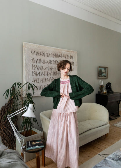 Milhazes Cardigan: green knit cardigan layered over a pink dress, photographed in a living room with abstract wall art and cozy furnishings.