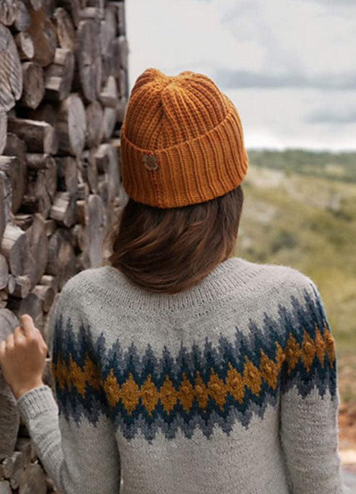 Back view of Rambla Sweater with zigzag stripes in blue and mustard on a light grey base, worn outdoors.
