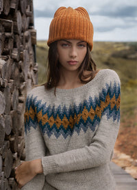 Rambla Sweater with blue and mustard zigzag pattern on light grey, worn outdoors with an orange knit hat.