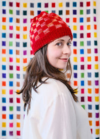 Side view of a Red Planet Hat with multicoloured checkered design, worn against a vibrant square-patterned backdrop.