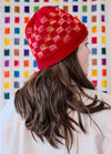 Angled view of a Red Planet Hat with geometric colourwork, shown in front of a colourful wall.