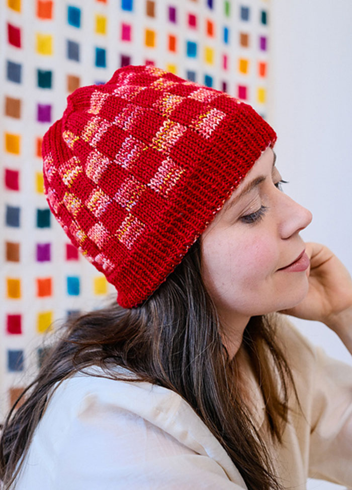 Front view of a Red Planet Hat with pink, orange, and yellow checkerboard pattern, displayed on a bright grid background.