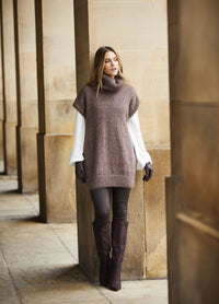 Woman in a cozy brown sleeveless sweater over a white shirt with gloves, leggings, and knee-high boots walks through a stone corridor, expressing calm elegance.