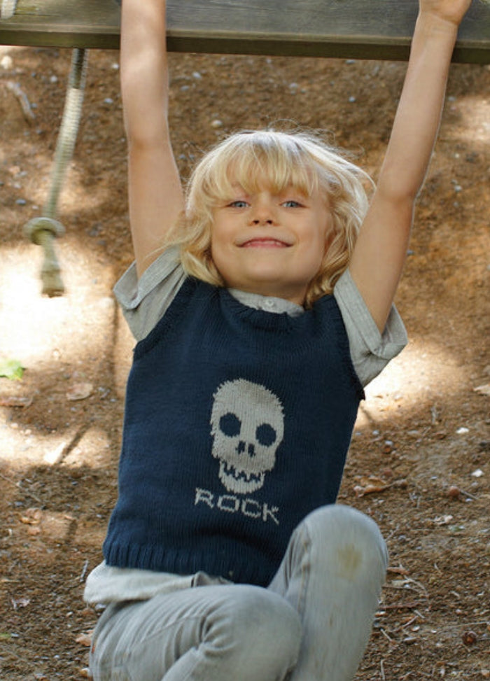 Child in dark blue sleeveless Rock Sweater with skull motif, hanging from playground equipment.