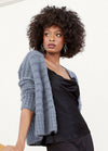 Woman with curly hair wearing a textured gray cardigan over a black satin blouse. She looks to the side with a confident, thoughtful expression.