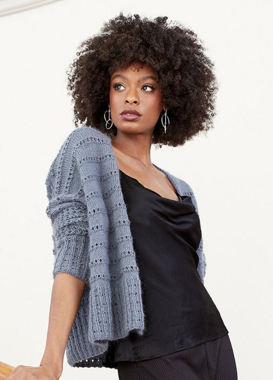 Woman with curly hair wearing a textured gray cardigan over a black satin blouse. She looks to the side with a confident, thoughtful expression.