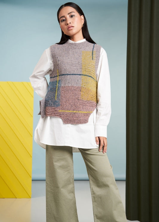 A woman stands confidently in a modern outfit with a textured vest over a white shirt and beige pants. The background features a yellow panel and green curtain.