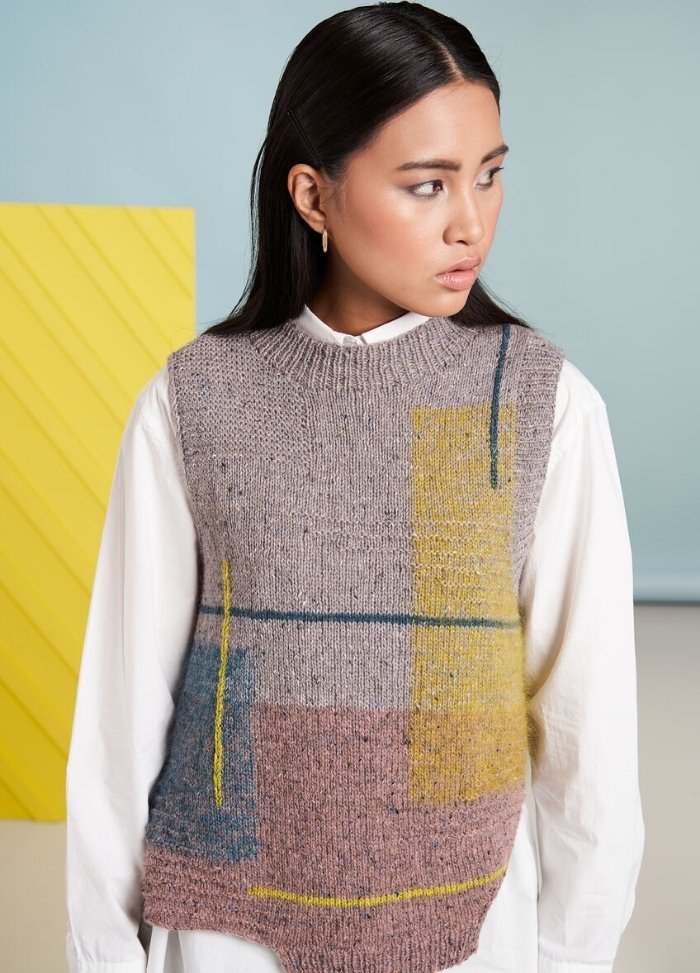 A woman with long dark hair looks to the side wearing a white blouse and a geometric-patterned, sleeveless knit vest in muted colors. The background is light blue and yellow, creating a modern, stylish tone.