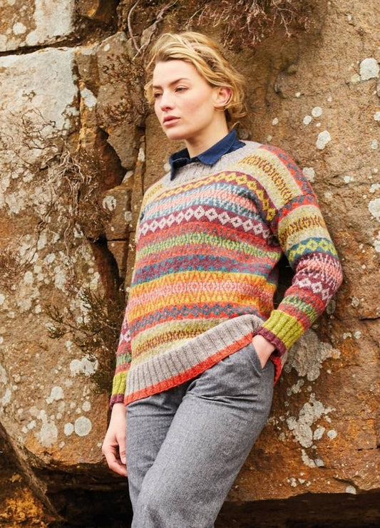 Person in a colorful patterned sweater and gray pants leans against a textured rock wall, expressing a calm and introspective mood in natural surroundings.