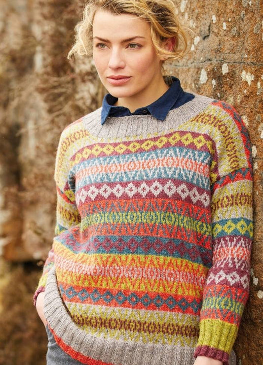 Woman in a colorful, patterned sweater with a blue collar, leaning against a textured stone wall. Her expression is calm and contemplative.