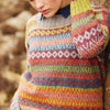 A person with blonde hair leans against a stone wall, wearing a colorful, patterned knit sweater. The expression is thoughtful, creating a calm and introspective mood.