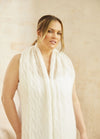 Woman with light brown hair wears a soft white knitted scarf against a beige background. Her expression is calm, adding to the serene mood.