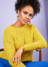 Woman wearing a bright yellow knit sweater and blue pants, sitting on a wooden chair with a soft purple backdrop. Her expression is calm and confident.