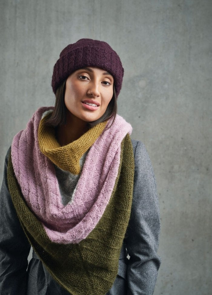 Woman in a stylish gray coat, wearing a maroon knitted hat and a multi-colored scarf in pastel pink, mustard, and olive. Concrete background.