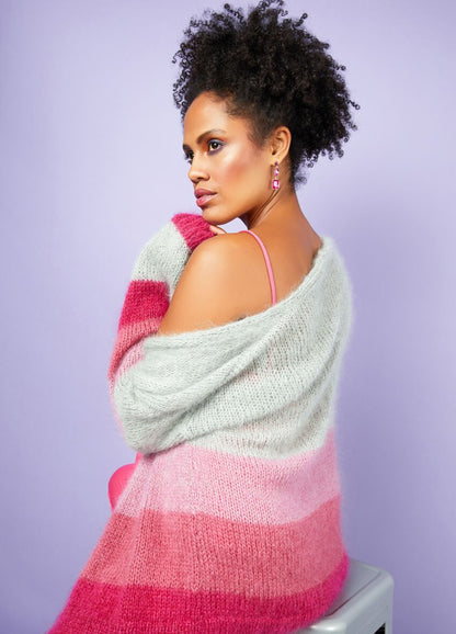 Woman with curly hair in a pink-and-white striped sweater sits against a pastel purple background, exuding confidence and elegance.