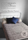 A metal-framed bed features a detailed crochet blanket with circular and square patterns. Two pillows, one dark blue, add contrast. Text reads "Beneath the Surface: Crochet Blanket Pattern by Shelley Husband" in UK terms. The scene feels cozy and inviting.