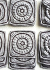 Gray crochet squares with intricate circular patterns are neatly stacked in rows, showcasing the textured craftsmanship and creating a sense of orderly repetition.