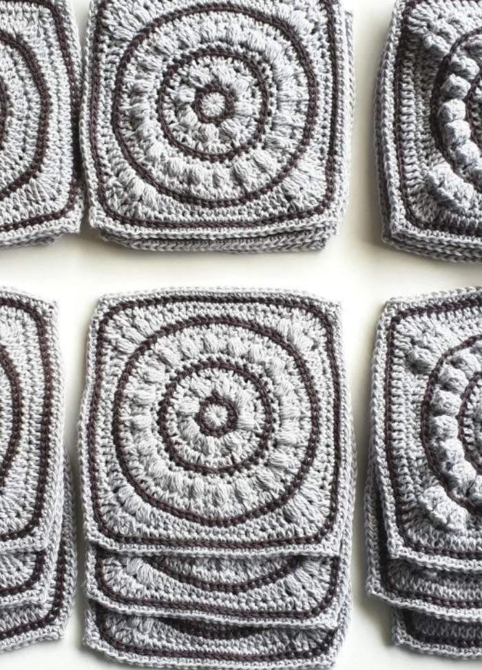 Gray crochet squares with intricate circular patterns are neatly stacked in rows, showcasing the textured craftsmanship and creating a sense of orderly repetition.