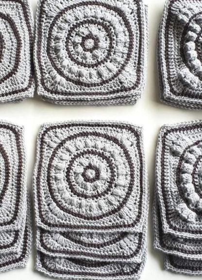 Gray crochet squares with intricate circular patterns are neatly stacked in rows, showcasing the textured craftsmanship and creating a sense of orderly repetition.