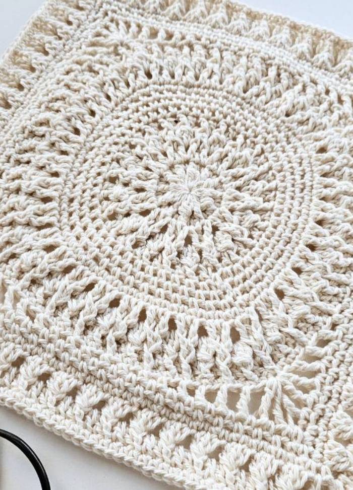 A detailed, cream-colored crocheted square with intricate circular patterns and textured edges, conveying a sense of warmth and craftsmanship.