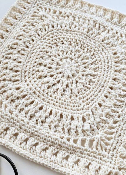 A detailed, cream-colored crocheted square with intricate circular patterns and textured edges, conveying a sense of warmth and craftsmanship.
