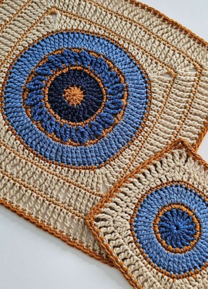 Close-up of two crocheted doilies with concentric circles in blue, cream, and brown. The texture is detailed, creating a cozy, artisanal feel.