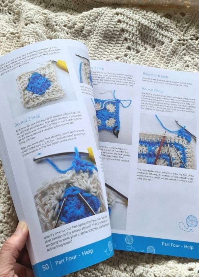 Open crochet instruction book on a textured knitted blanket. Pages show step-by-step guides with images of blue and white crochet squares.
