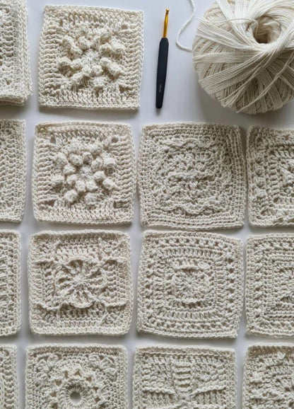 A collection of intricately crocheted white squares, each with unique patterns, arranged neatly. A crochet hook and yarn ball are visible, suggesting crafting in progress.