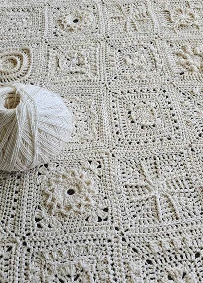A detailed crochet blanket made from cream-colored yarn squares, each with unique patterns. A yarn ball sits on top, showcasing intricate craftsmanship.