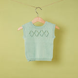 Green knitted sleeveless sweater on a hanger against a green background