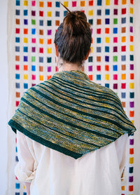 Striped Saturn Shawl in green, yellow, and blue, worn over shoulders, with a colorful grid background.