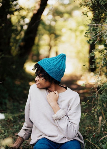 Blue knit cap worn outdoors with a light long-sleeve shirt, surrounded by greenery.