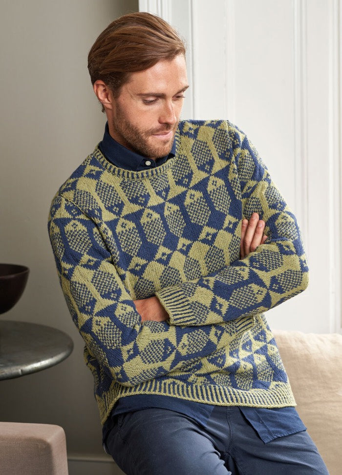 A man in a cozy sweater featuring bold geometric patterns in shades of blue, red, and white, showcasing intricate knitwork.