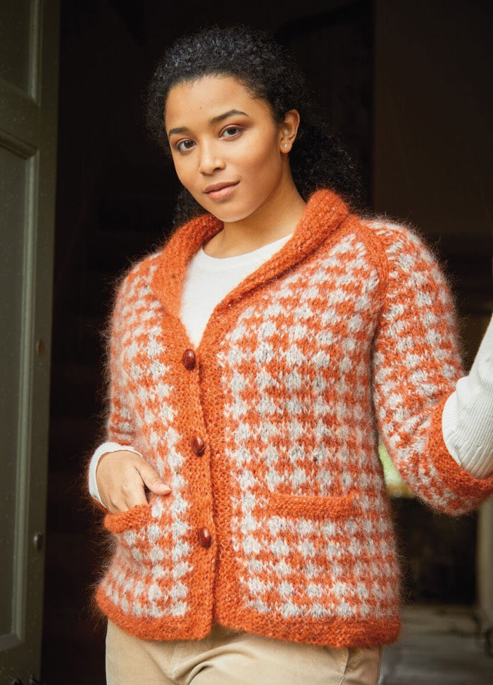 A person poses confidently in a cozy, orange and white checkered knit cardigan with large buttons, conveying warmth and style.