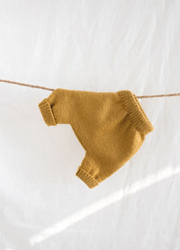 A pair of mustard yellow, knitted children's pants hangs on a string against a white background. The soft texture creates a warm, cozy feel.