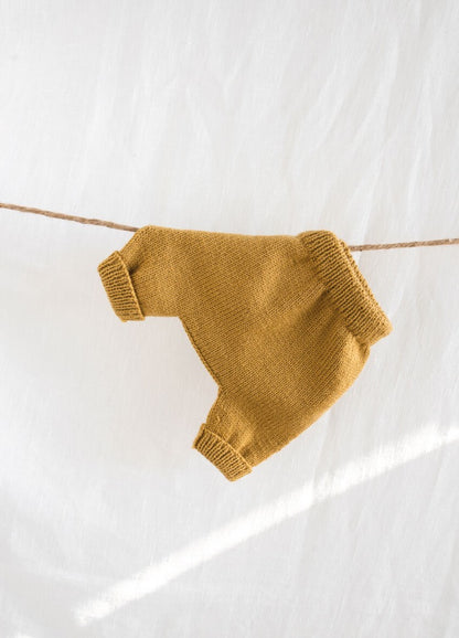 A pair of mustard yellow, knitted children's pants hangs on a string against a white background. The soft texture creates a warm, cozy feel.
