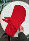 A person holding a vibrant red, knitted scarf on a round, marble table with a gold rim.
