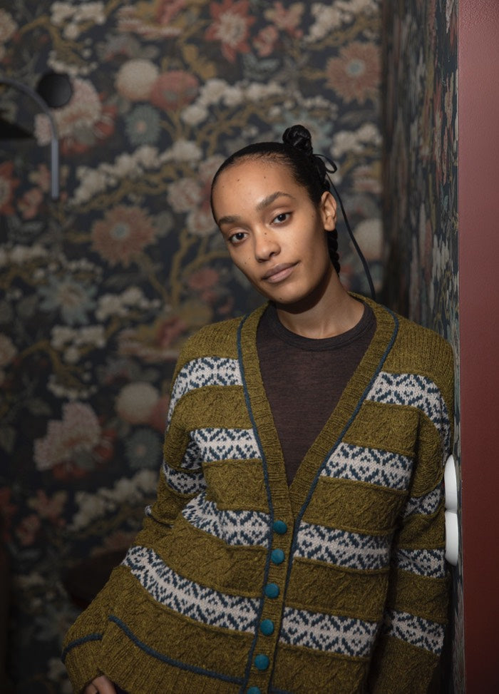 Crocodile Line Cardigan: green and white striped knit with blue geometric accents and blue buttons, set against floral wallpaper.