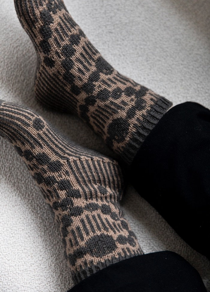 Grandma's Pearls Socks: gray and beige knit socks with vertical stripes and pearl-like circular motifs, worn with black pants.