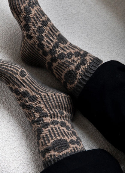 Grandma's Pearls Socks: gray and beige knit socks with vertical stripes and pearl-like circular motifs, worn with black pants.