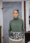 Rascal Spirit Sweater: green high-neck knit with black and white abstract animal print near hem, shown against a wooden door.