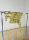 Green and white striped knitted sweater with large buttons, creatively draped over a metal clothing rack against a beige panelled wall.