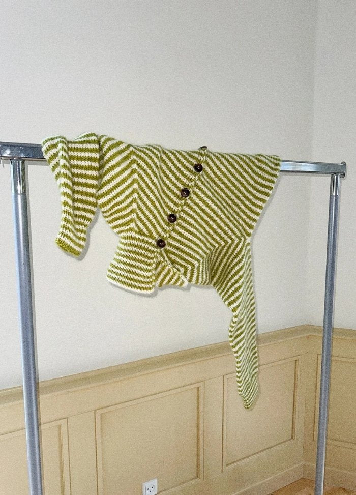 Green and white striped knitted sweater with large buttons, creatively draped over a metal clothing rack against a beige panelled wall.