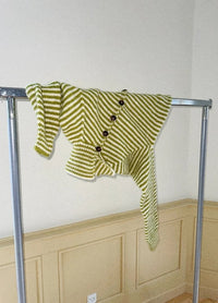 Green and white striped knitted sweater with large buttons, creatively draped over a metal clothing rack against a beige panelled wall.