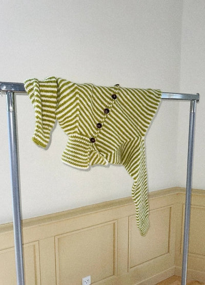 Green and white striped knitted sweater with large buttons, creatively draped over a metal clothing rack against a beige panelled wall.