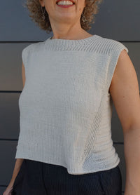 Woman wearing sleeveless Summer Esio Top in a soft neutral tone, hand-knitted with lightweight yarn. Features ribbed trim at neckline and armholes, perfect for warm-weather layering or standalone wear.