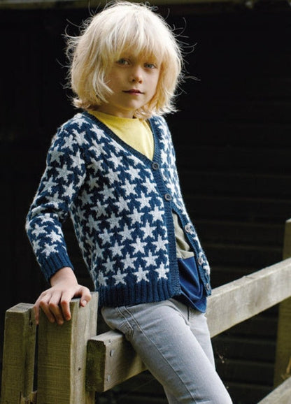 Child in blue Sundance Cardigan with white stars, yellow shirt, and light pants, by fence.