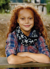 Child in Sundance Cowl with star motif over plaid shirt, outdoors with greenery.