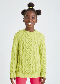 A smiling child wearing a bright yellow cable-knit sweater and red pants stands against a plain background. They convey a joyful and cheerful vibe.