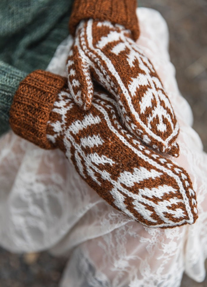 Suolaulu Mittens: brown knit mittens with white traditional motifs, worn with a green sweater and white lace skirt.